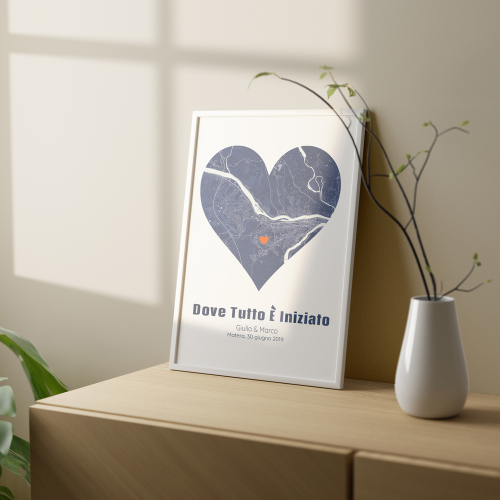 Mappa blu a forma di cuore in cornice bianca, appoggiata su un mobile in legno accanto a un vaso